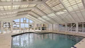 An indoor swimming pool with clear glass ceilings, lounge chairs, and a view of the outdoors.