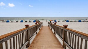 A wooden boardwalk leading to a beach with umbrellas and lounge chairs.