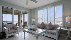 A spacious living room with a glass-top coffee table, a sofa with colorful cushions, and a view of the beach through large windows.