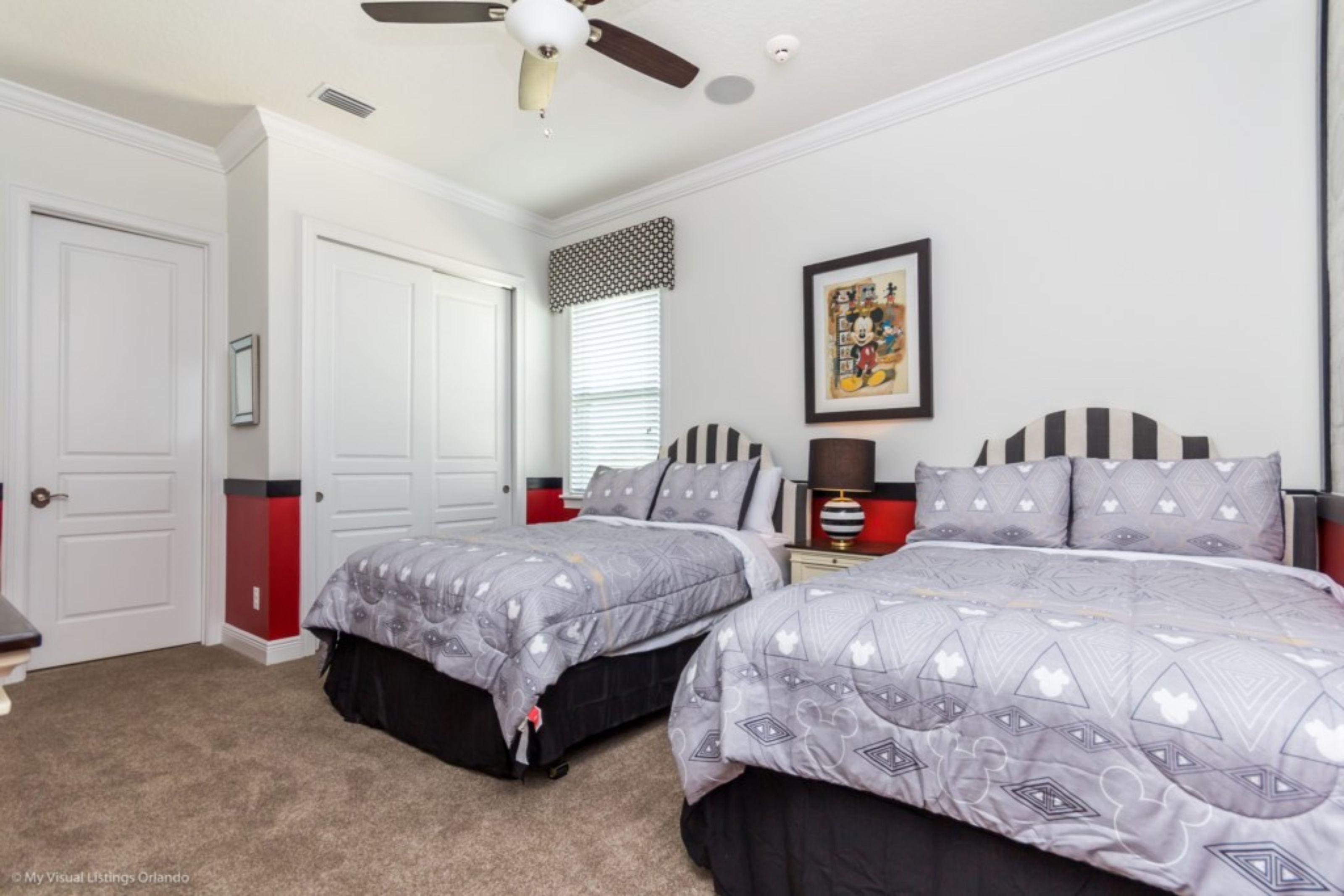 Une chambre avec deux lits, un ventilateur de plafond, une fenêtre avec des stores et un tableau encadré au mur.