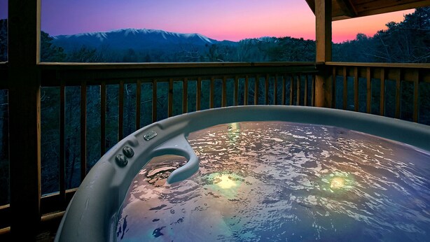 Un jacuzzi con vista a una cadena montañosa al atardecer.