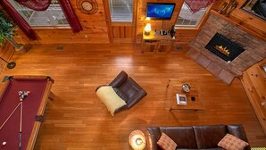 Una cabaña de madera acogedora con mesa de billar, sofás de cuero, chimenea y televisión.