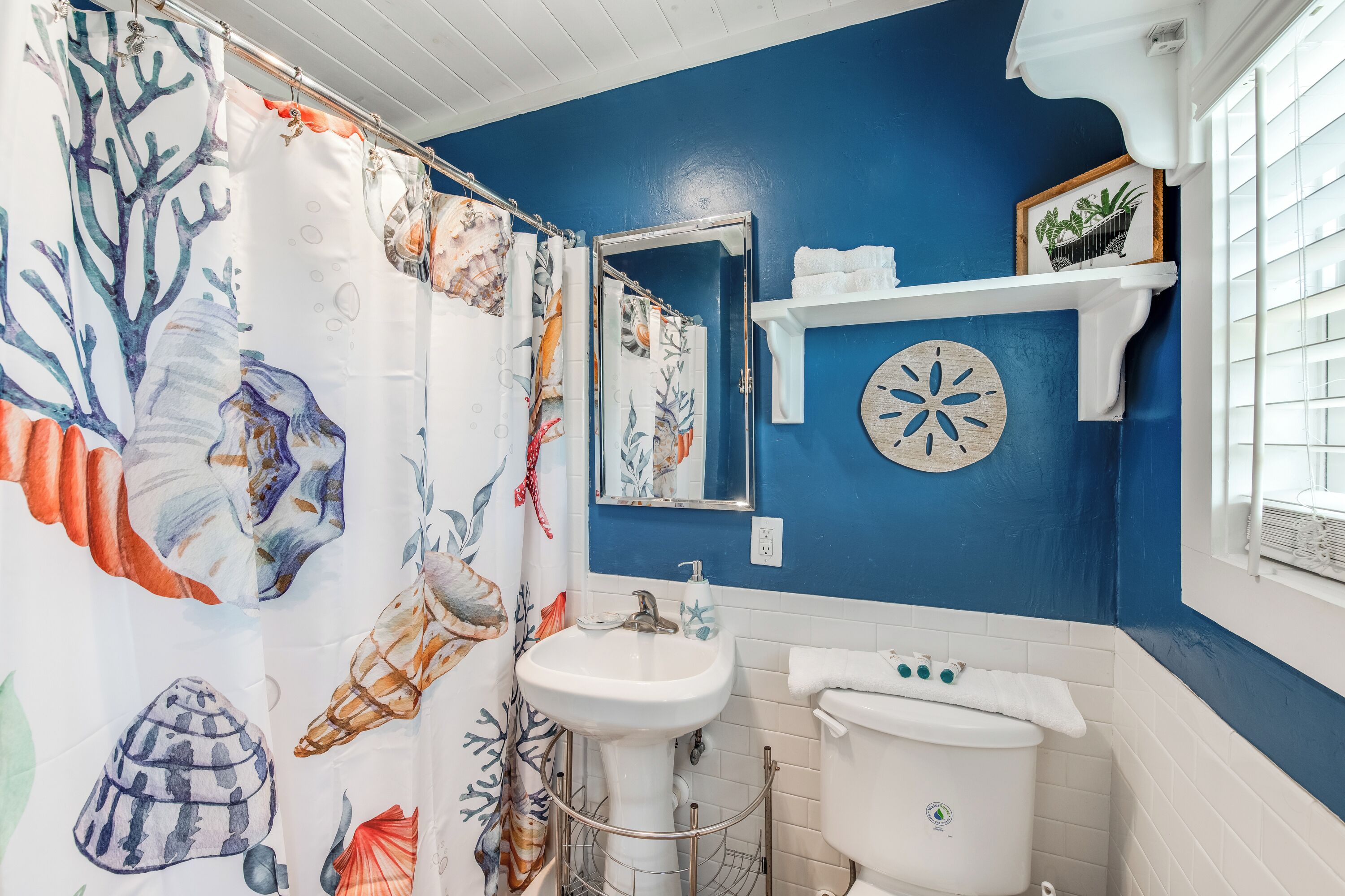 A bathroom with a blue wall, white sink, and toilet. There is a shower curtain with a sea shell pattern.