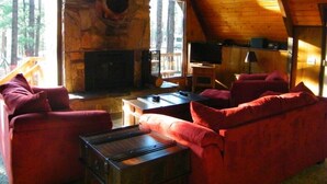 A log cabin interior with a stone fireplace, red upholstered furniture, and a television.