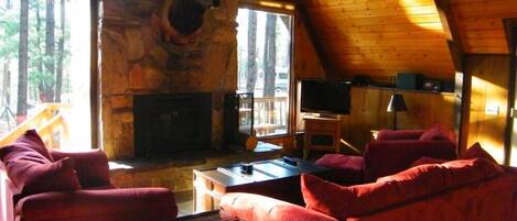 A log cabin interior with a stone fireplace, red upholstered furniture, and a television.