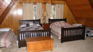 A cozy attic bedroom with two wooden beds, a nightstand, and a small wooden bench.