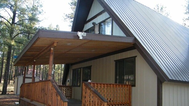 A cabin with a wooden porch, a metal roof, and a window.
