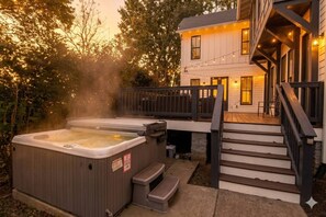A hot tub, stairs, and a house with a deck and string lights.
