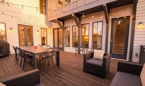 Una terraza al aire libre con una mesa de comedor y sillas, muebles de mimbre y luces colgantes.