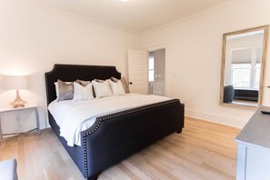 A bedroom with a bed, bedside table, lamp, and a mirror.