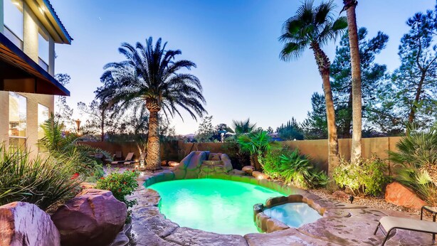 A swimming pool with a stone border, surrounded by palm trees and large rocks. - 5 STAR ⭐️⭐️⭐️⭐️⭐️ STUNNING PRIVATE LV ESTATE! (Las Vegas)