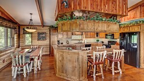 Una cocina de estilo rústico tipo cabaña, con armarios de madera, una isla central y un comedor con sillas de madera.