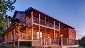 Una cabaña de troncos de dos pisos con un balcón, un porche y una escalera que conduce al nivel superior.