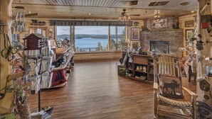 Un interior de cabaña acogedor con piso de madera, chimenea y una vista panorámica a un lago.