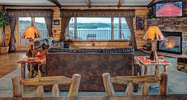 Et hyggeligt sommerhusinteriør med en stor sofa, træstole, en pejs og et fjernsyn.