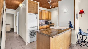 Una cocina compacta con armarios de madera, microondas integrado, lavadora y encimera de granito.