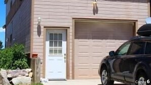 Une maison à deux étages avec un balcon, un garage et un VUS garé devant.