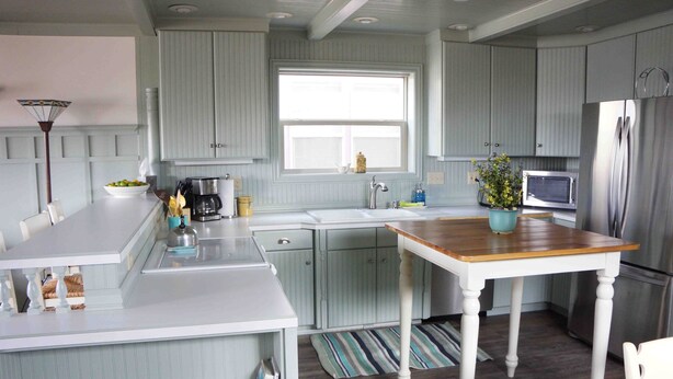 Une cuisine avec des meubles de couleur bleu clair, une table en bois, un évier, un four à micro-ondes et un réfrigérateur.