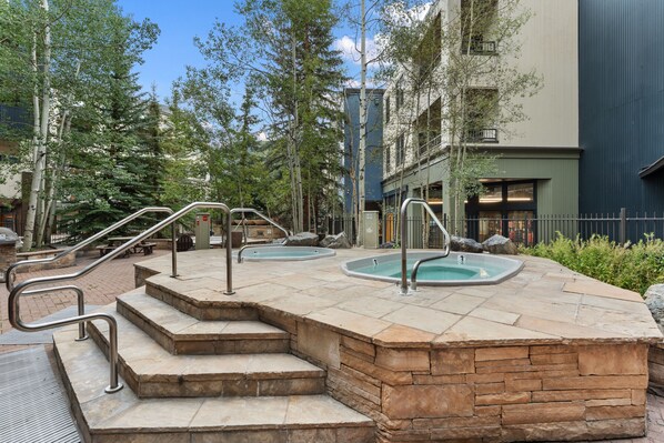 A pool area with steps leading to the pool, surrounded by trees and a building.