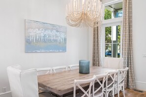 A dining area with a wooden table, white chairs, a blue vase, and a painting on the wall. - Luxury 3-story WaterColor Home. Private Pool, Bikes, Golf Cart, Lots of Amenities. Ideal for Groups! (Santa Rosa Beach)