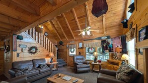 A cozy cabin interior with a wooden ceiling, a fireplace, a sofa, a coffee table, and a television. - ER245 – Almost Heaven  Great Location – Close to town! (Pigeon Forge)