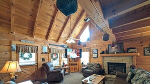 A cozy log cabin interior with a fireplace, leather sofas, and a television. - ER245 – Almost Heaven  Great Location – Close to town! (Pigeon Forge)