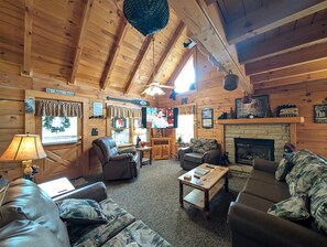 A cozy log cabin interior with a fireplace, leather sofas, and a television.