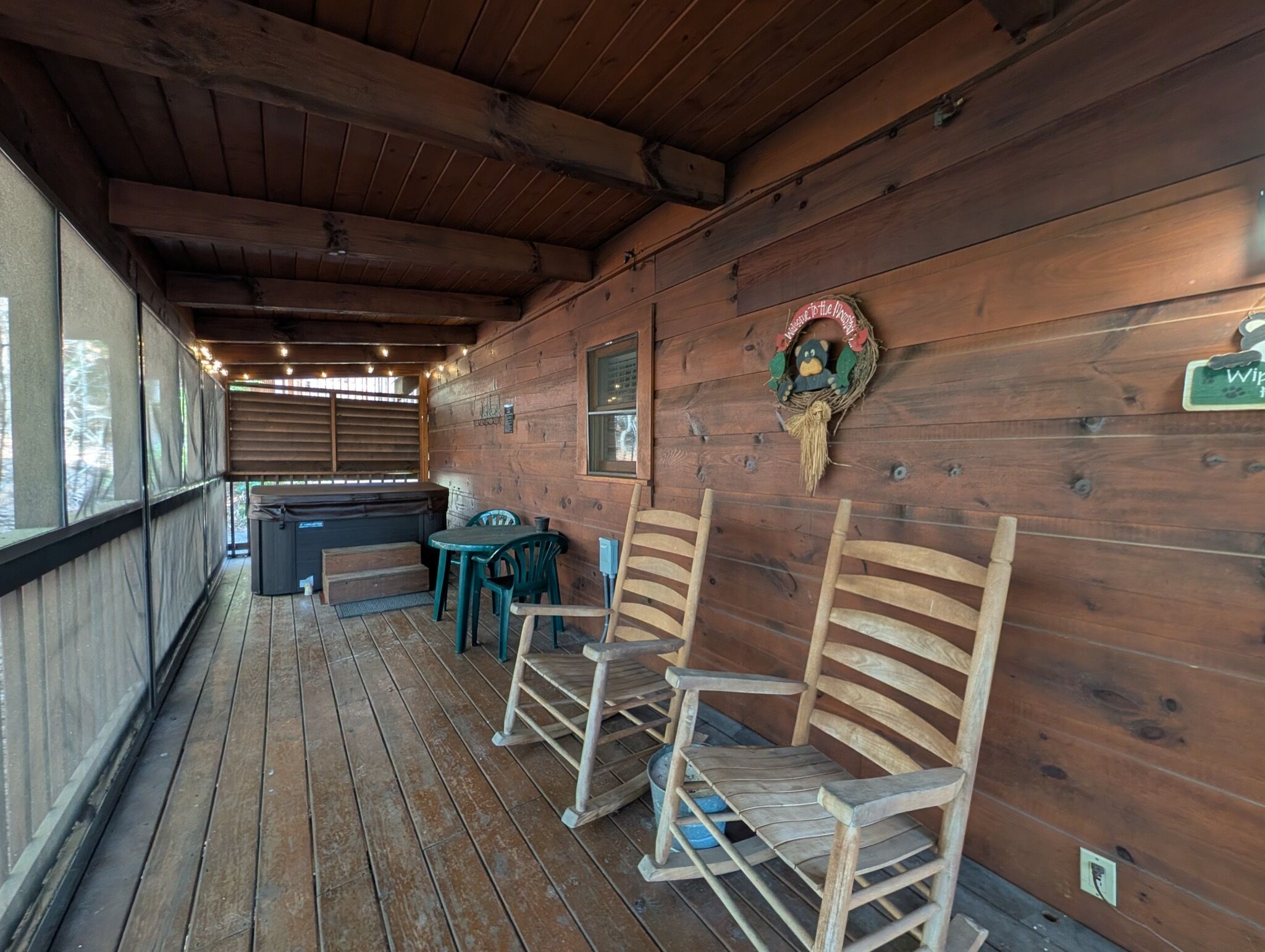 A wooden deck with a hot tub, wooden chairs, and a rustic wall with a decorative wreath.