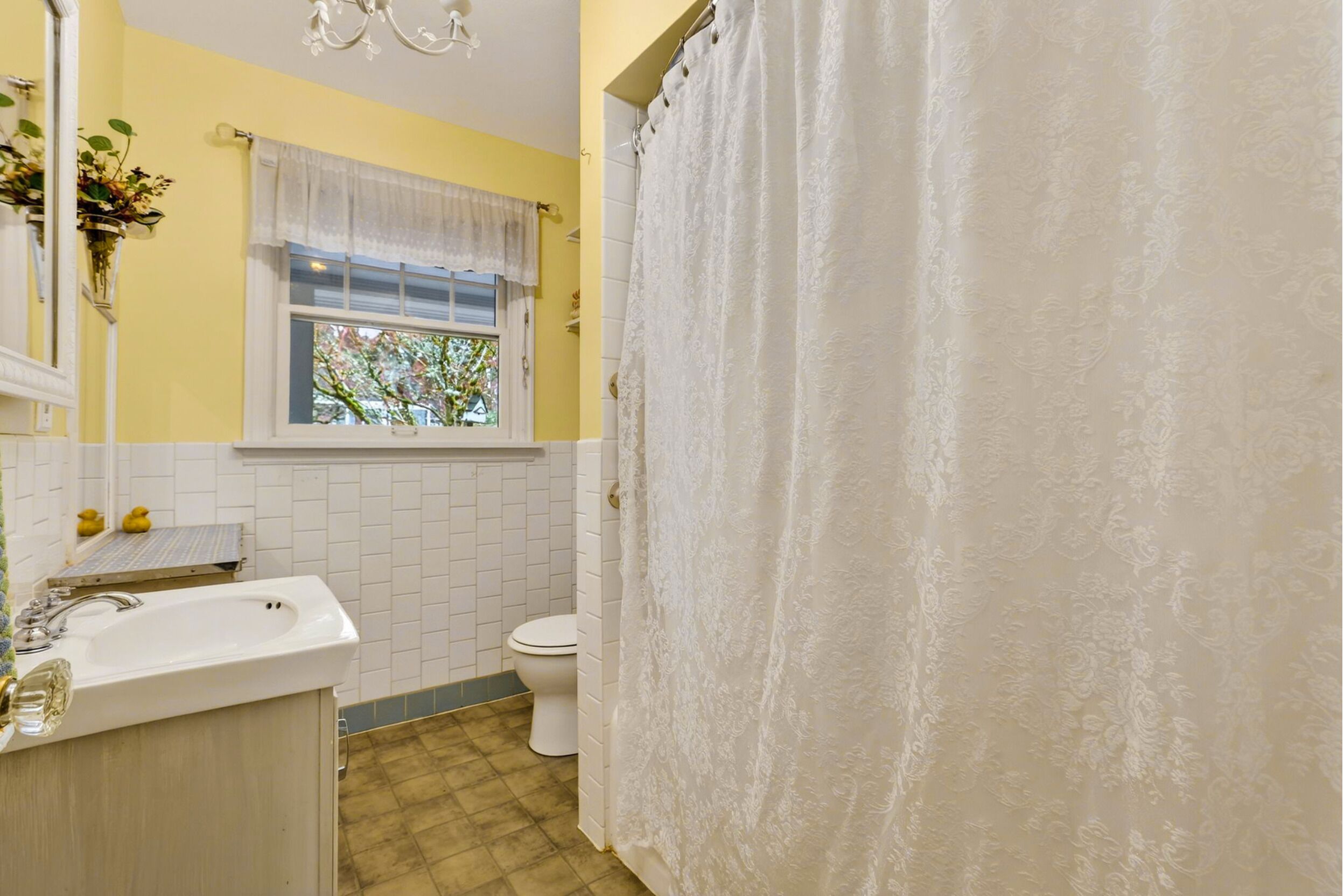 Ein Badezimmer mit Waschbecken, Toilette und Fenster mit weißem Vorhang.