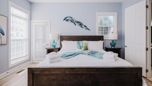 Un dormitorio con una cama grande, dos mesitas de noche con lámparas, una ventana con persianas y una puerta.