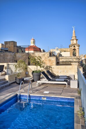 Piscina no terraço com vista para edifícios históricos e um campanário.