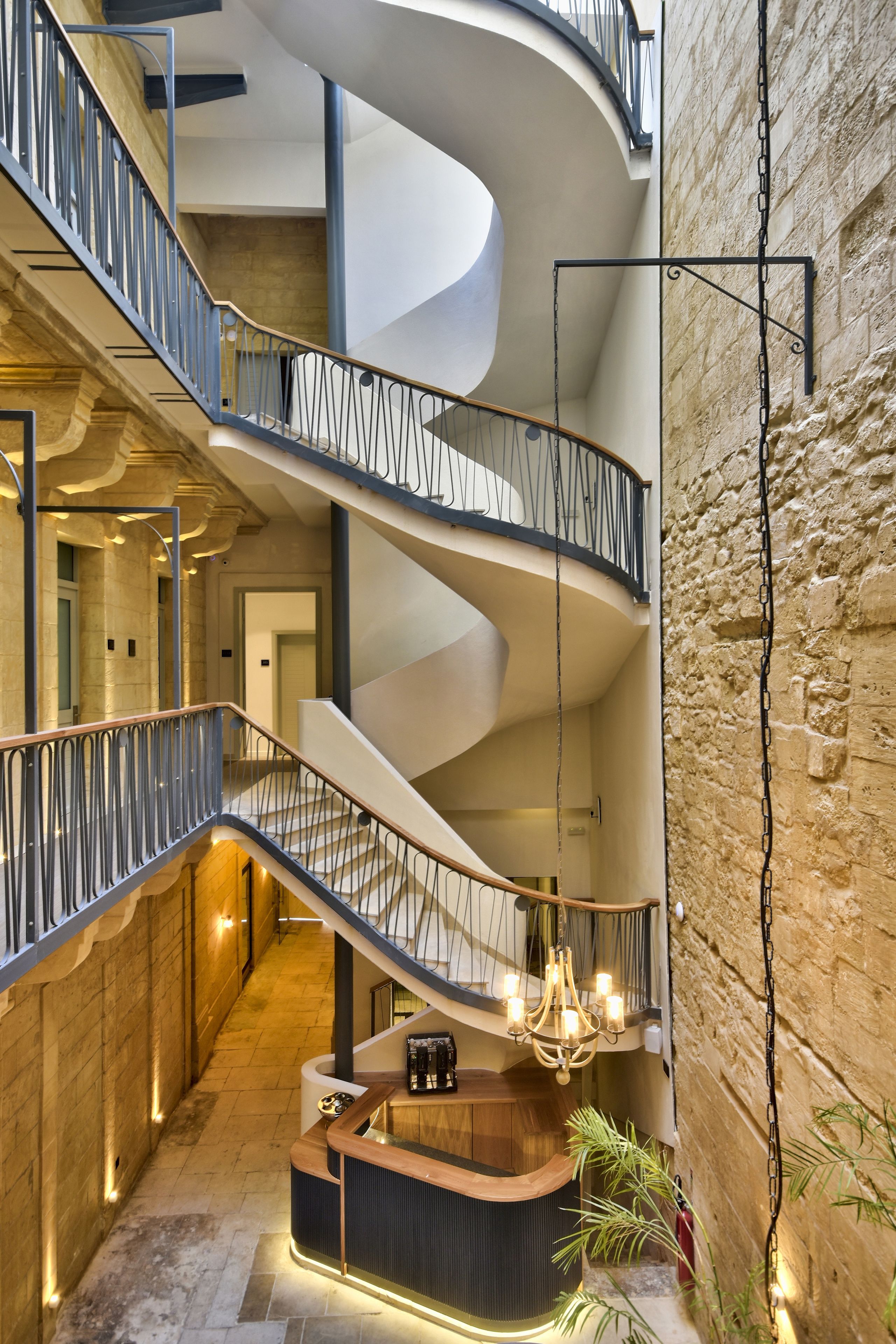 A multi-level interior with a central staircase, a reception desk, and a stone wall.