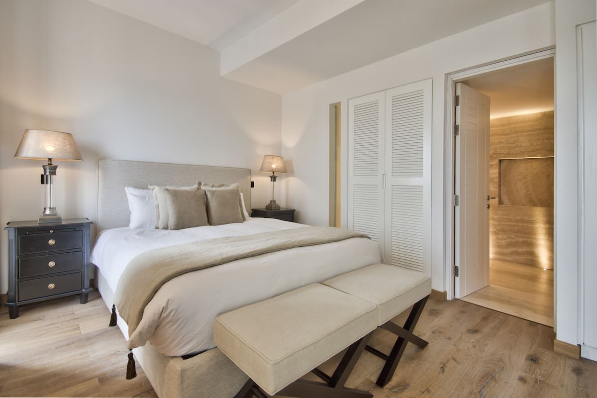 A bedroom with a large bed, bedside lamps, a bench, a nightstand, and a wardrobe.