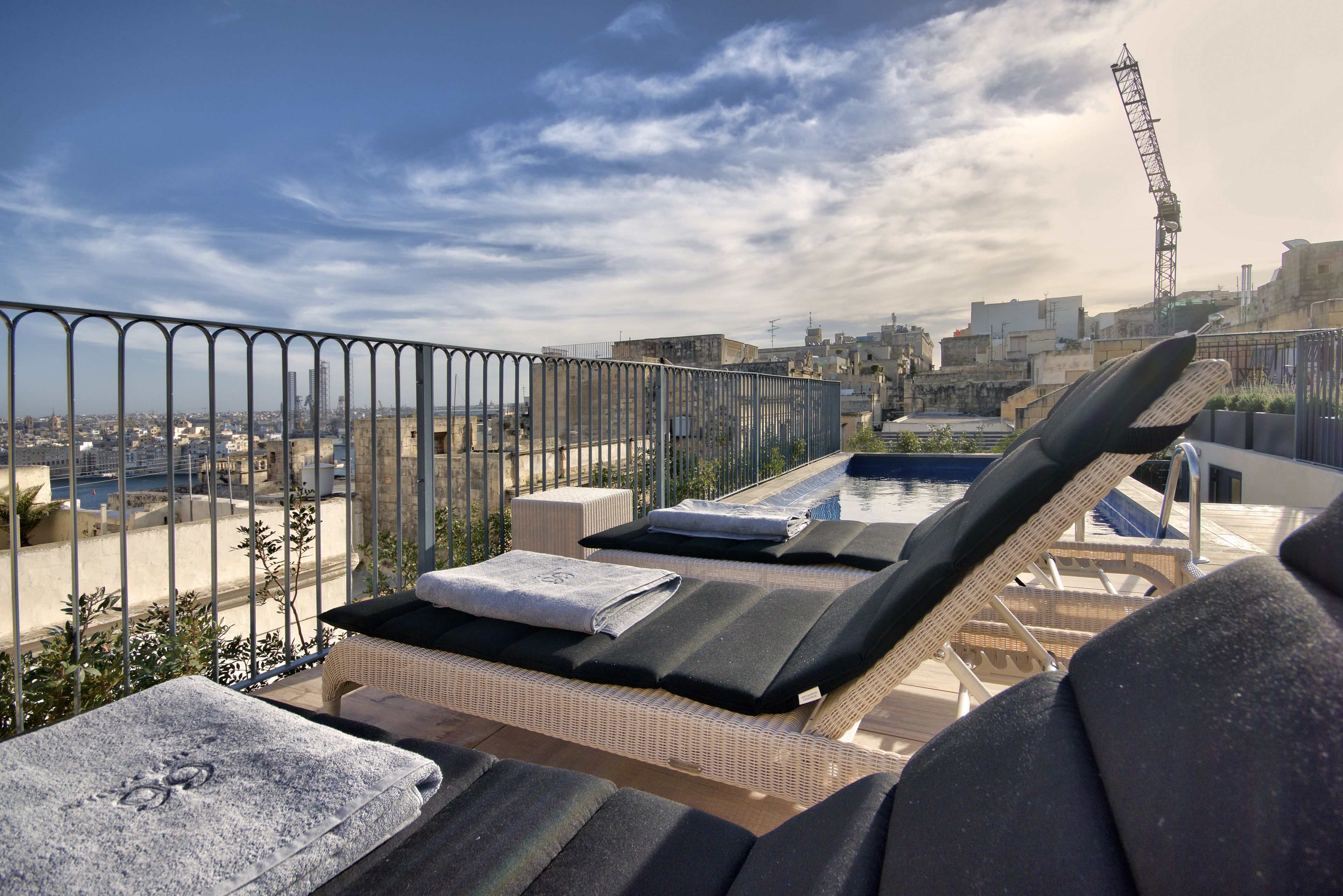 A rooftop lounge area with lounge chairs and a pool, overlooking a cityscape.