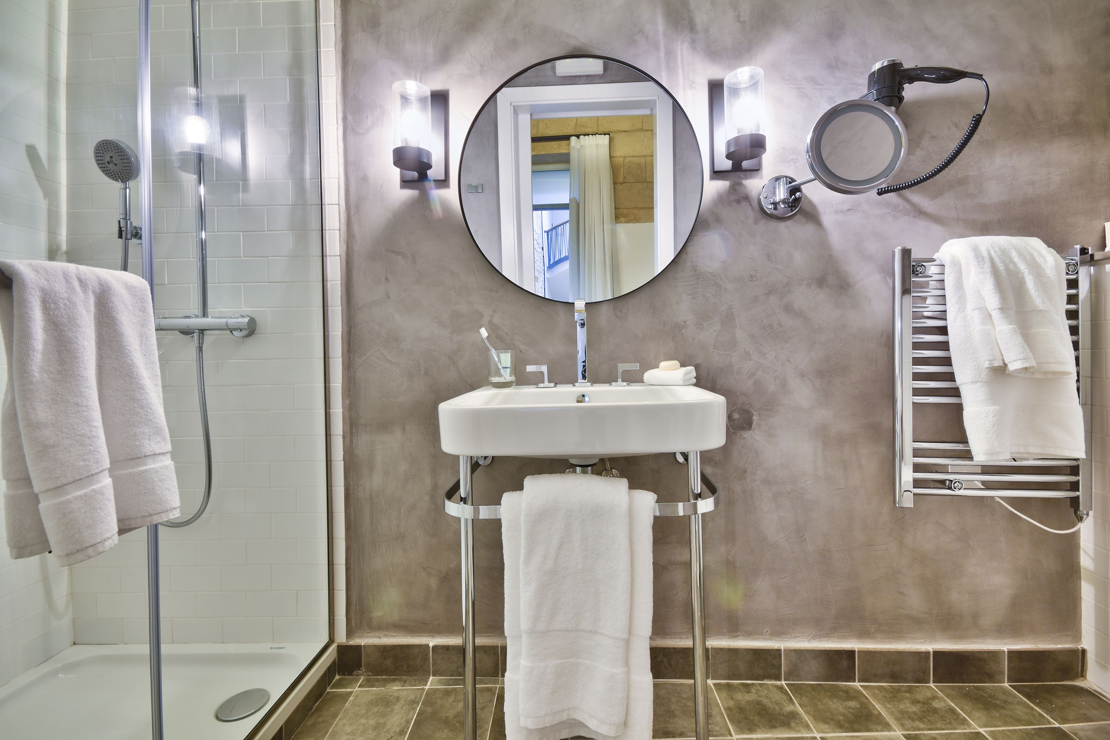 A bathroom with a shower, a sink, a mirror, and towel racks.