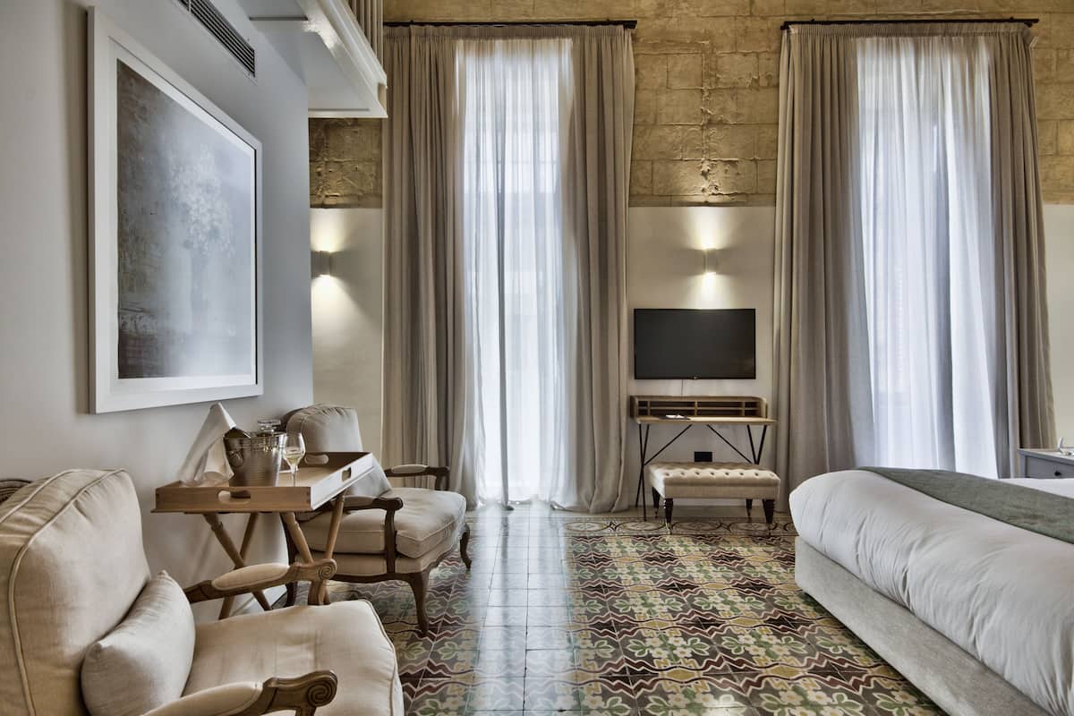 A hotel room with a large bed, a sofa, a TV, and a dining area with a table and chairs.