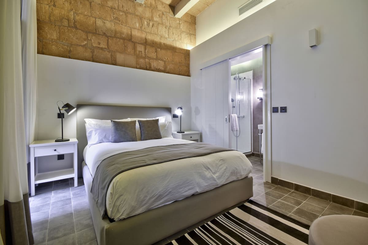 A modern bedroom with a large bed, bedside tables, a nightstand, a striped rug, and a brick ceiling.