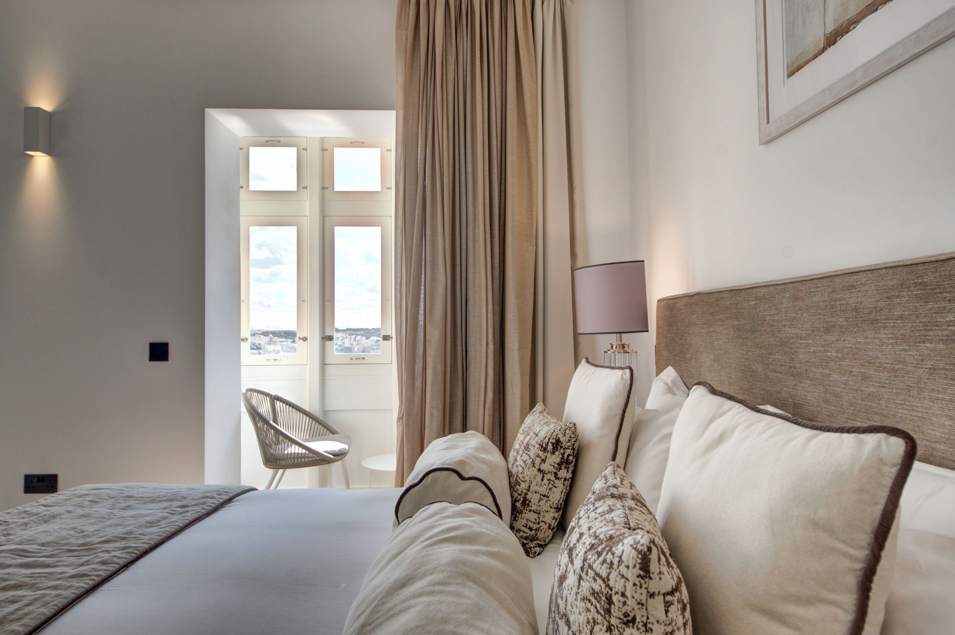 Een hotelkamer met een bed, een stoel, een lamp en uitzicht door een raam.