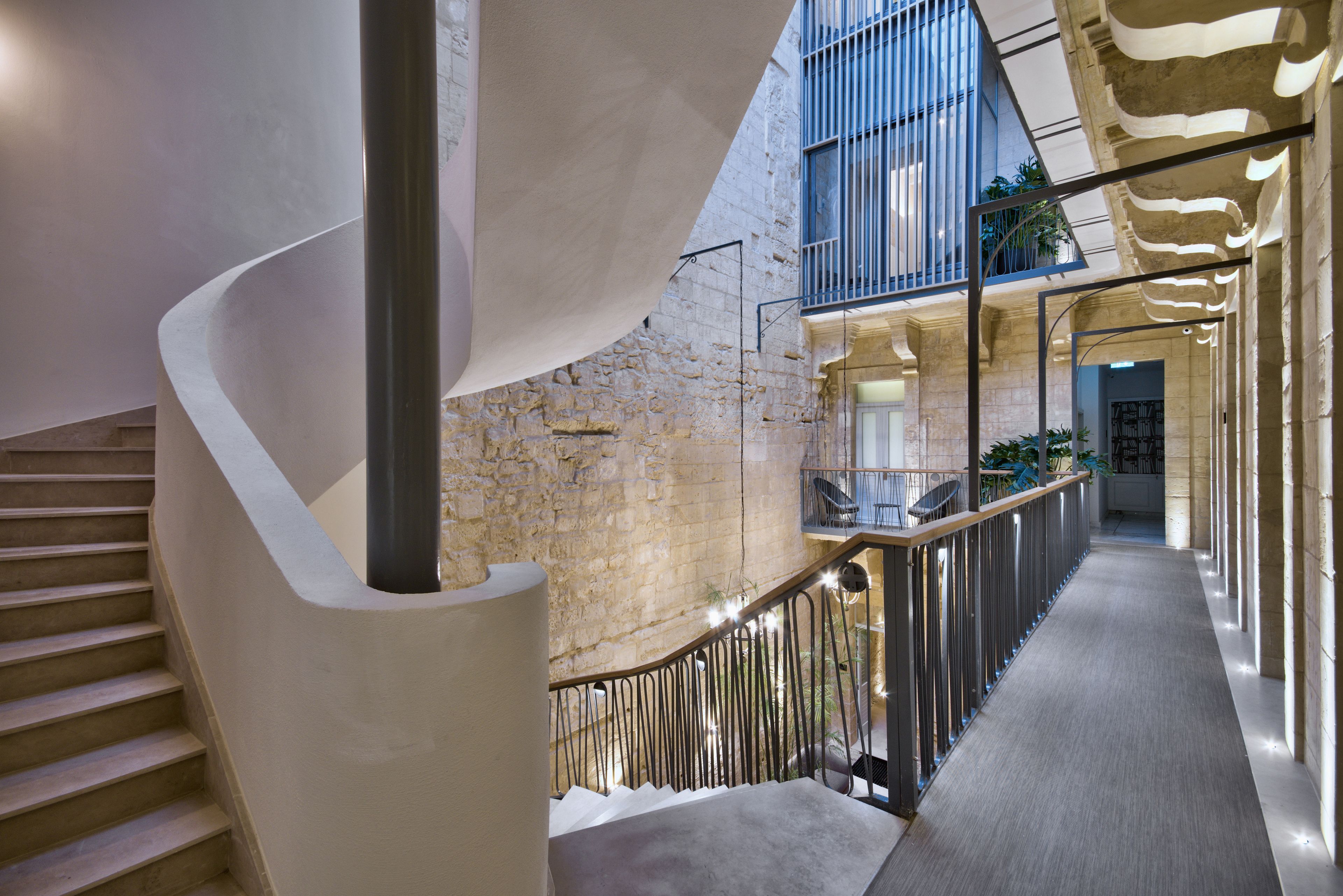 A modern interior with a curved staircase, a high ceiling, and a balcony with plants.