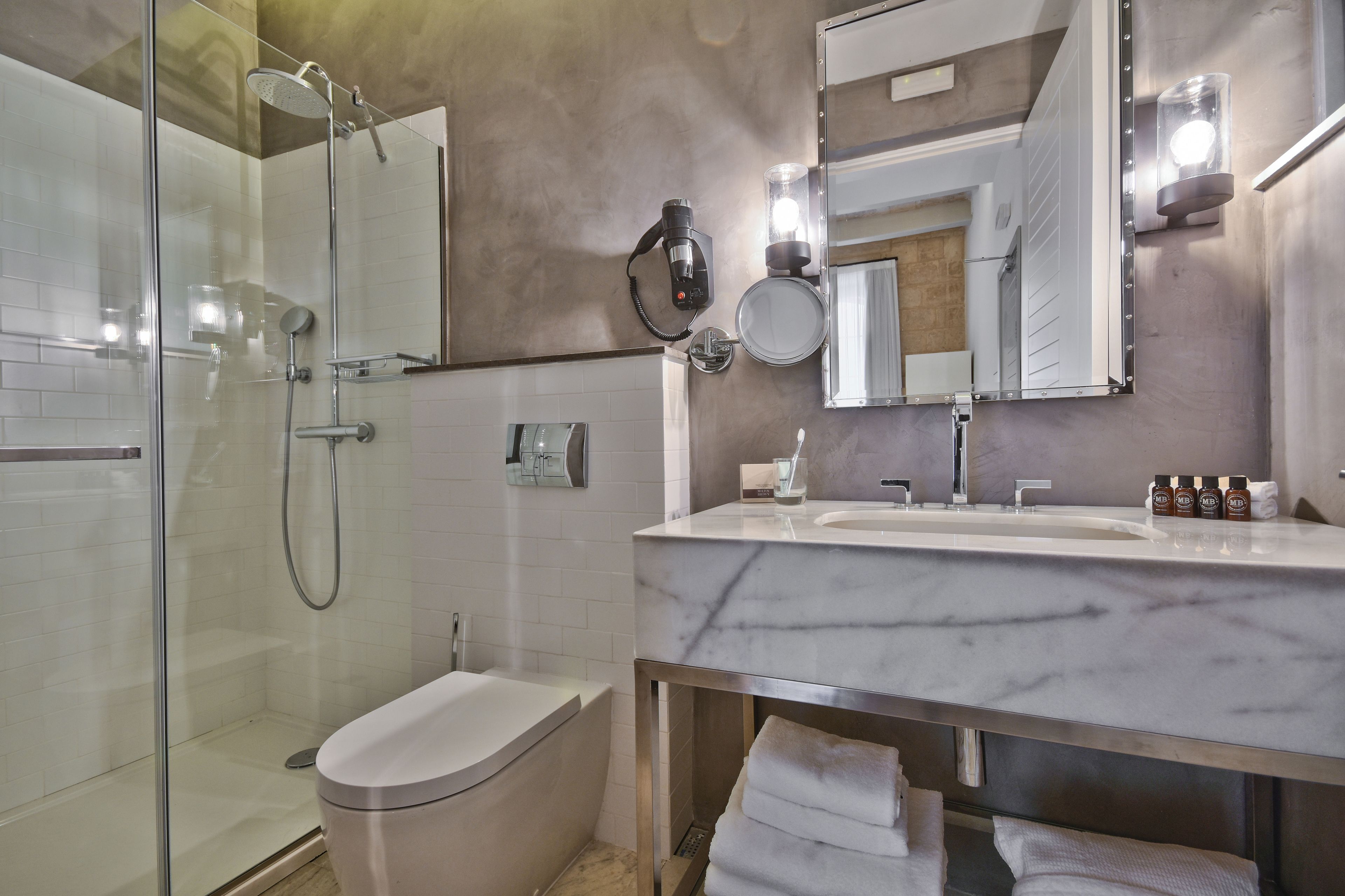 Une salle de bain moderne avec une douche à parois de verre, des toilettes blanches, un lavabo en marbre et un grand miroir.