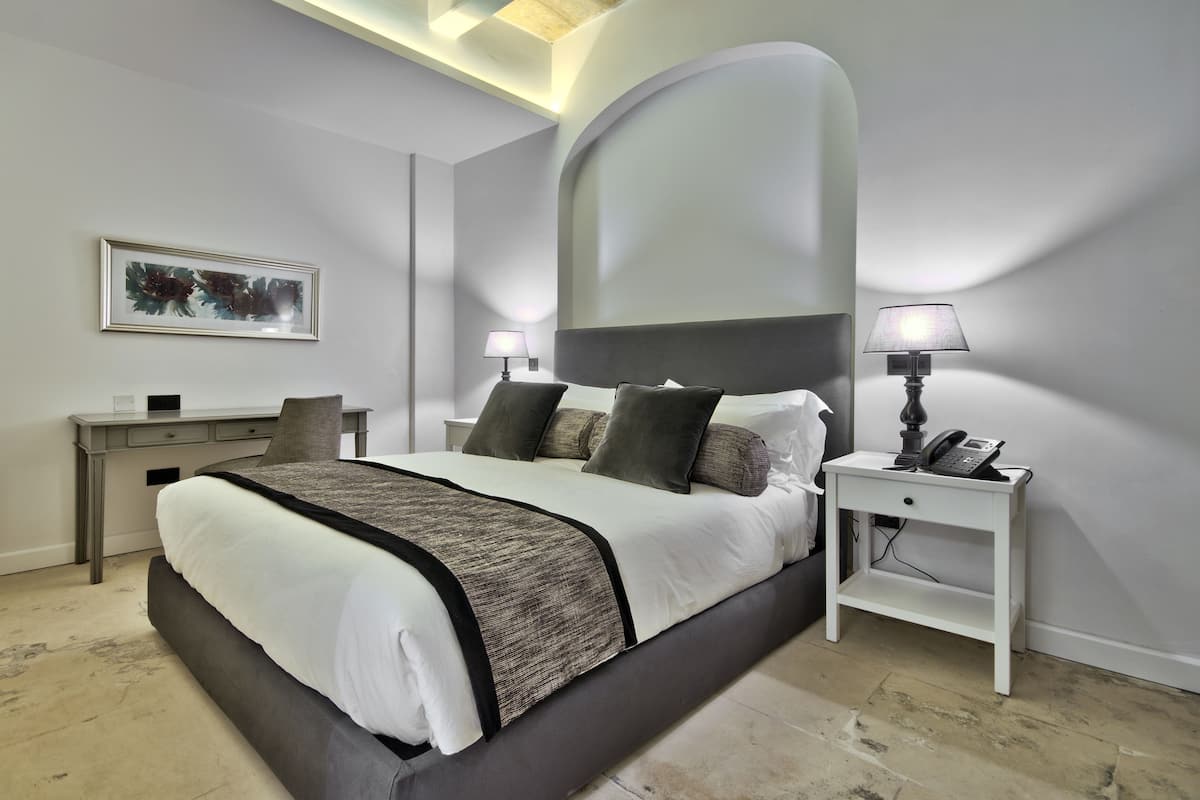 A modern bedroom with a large bed, bedside tables, a desk, and a framed picture on the wall.