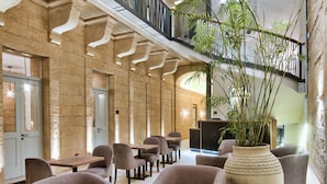 A spacious lobby with a high ceiling, a central seating area with sofas and chairs, a large potted plant, and a staircase leading to an upper level. - 66 Saint Pauls & Spa (Valletta)