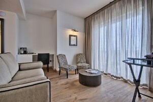 Una sala de estar moderna con un sofá, dos sillones con estampado de cebra, una mesa de centro redonda y una mesa de comedor con una silla. Se observa un cuadro en la pared y una pequeña zona de kitchenette al fondo.