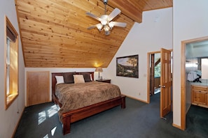 A bedroom with a wooden ceiling, a bed, a nightstand, a lamp, and a painting.