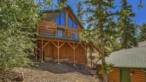 A two-story wooden cabin with a balcony, surrounded by trees.