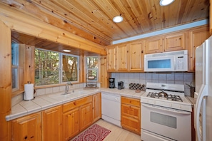 A kitchen with wooden cabinets, a white stove, a microwave, and a sink.