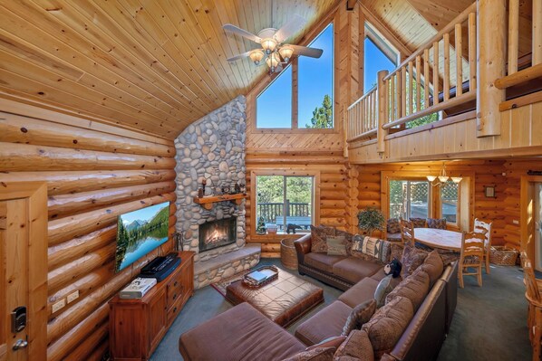 A log cabin interior with a fireplace, a television, a sofa, and a balcony.