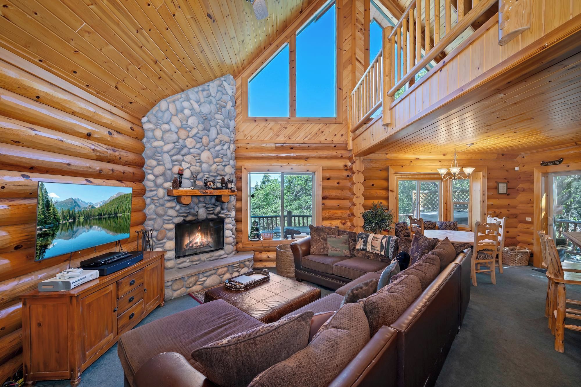 A log cabin interior with a stone fireplace, a large TV, and a cozy seating area.