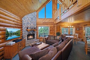 A log cabin interior with a stone fireplace, a large TV, and a cozy seating area.