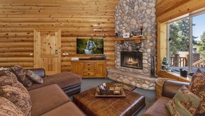 A log cabin interior with a stone fireplace, wooden walls, a television, and a cozy seating area.
